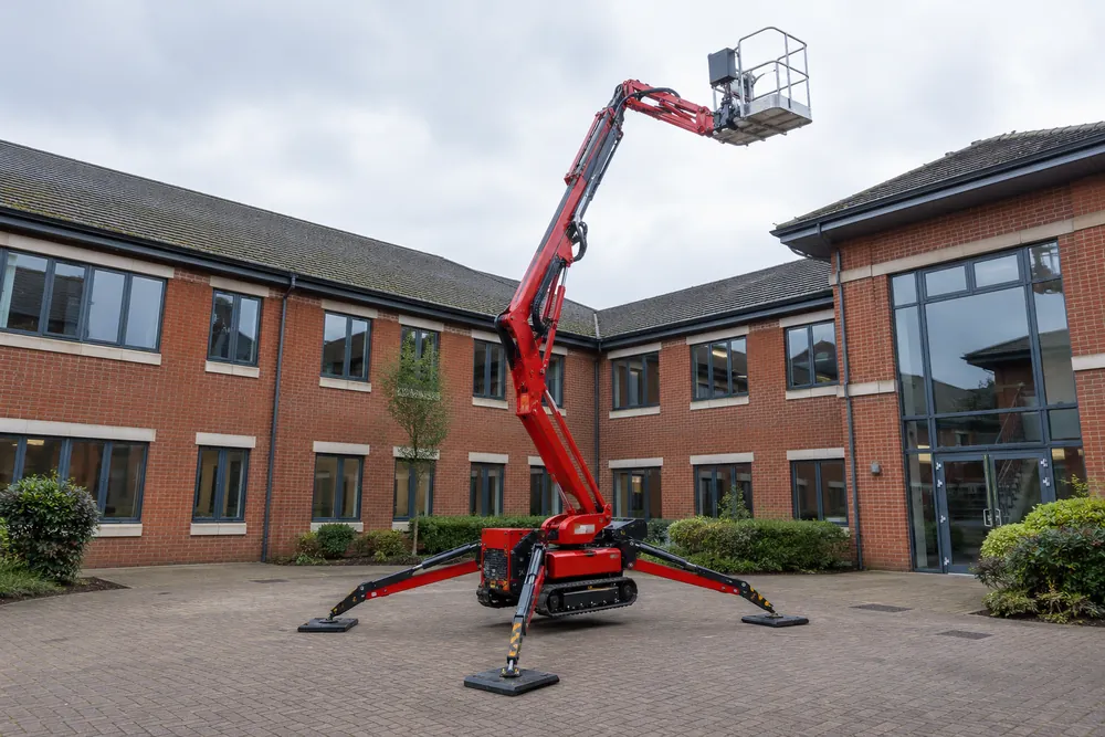 Tracked spider lift with deployed stabilisers in a brick commercial courtyard